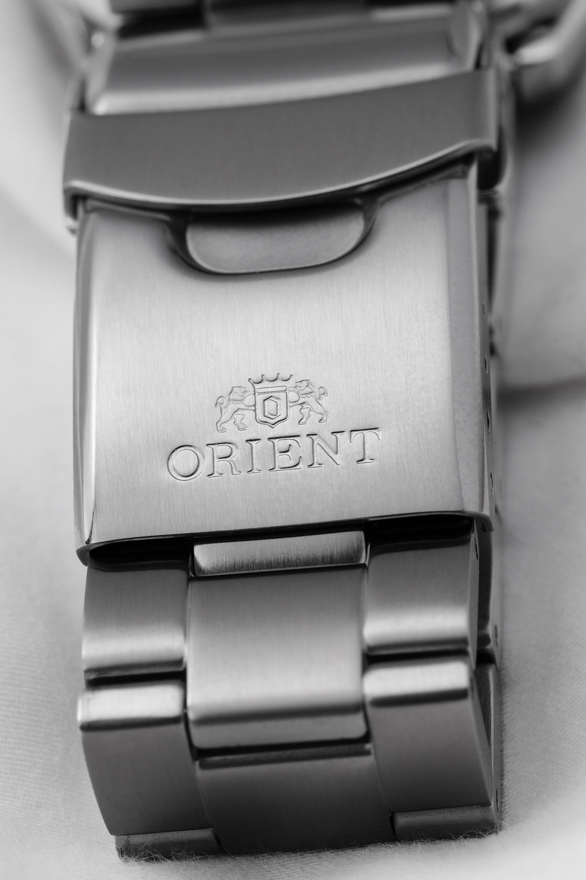Orient stainless steel watch bracelet with a brushed metal clasp featuring an engraved Orient logo and branding, shown in close-up.

Orient Kamasu RA-AA0001B39B