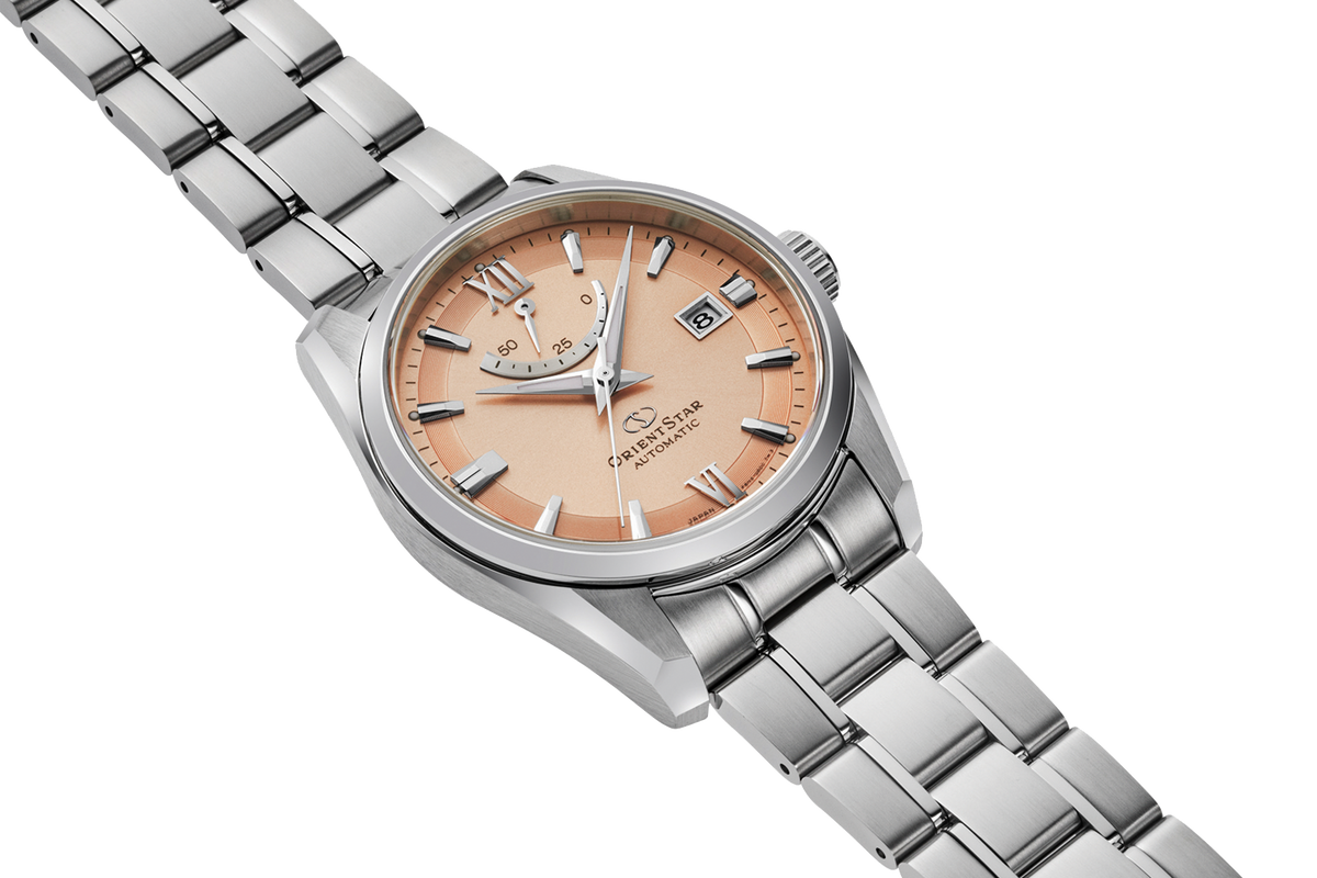 A wristwatch with a silver stainless steel link bracelet and a peach-colored dial, shown on a clean white background.

Orient Star RE-AU0108G
